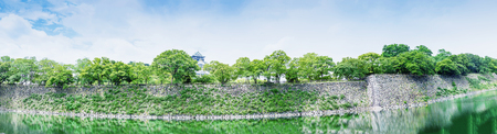 Panoramic view of Osaka Castle and walls surrounded by river.