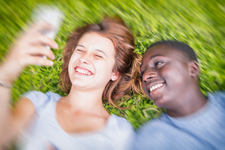 Afro american boy and caucasian girl laying on the grass happy making selfie