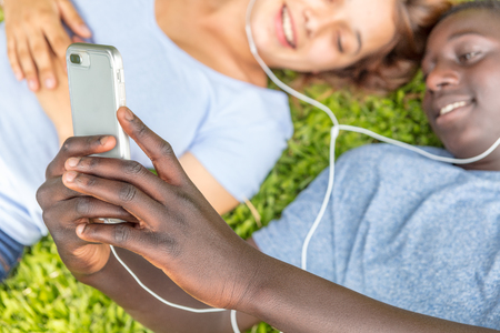 African boy and caucasian girl laying on the grass hearing music. Focus on the hands.の写真素材