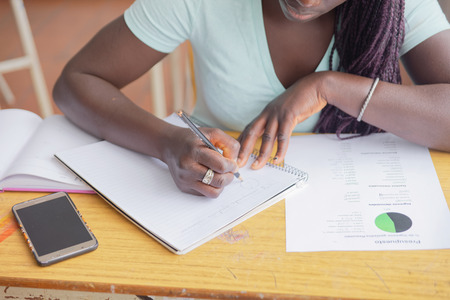 Afroamerican teenager girll making school test in the classroom using notebooks and smartphone.