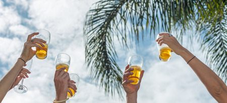 Drink and happiness concept. Beer glasses clinking up in the sky.の写真素材
