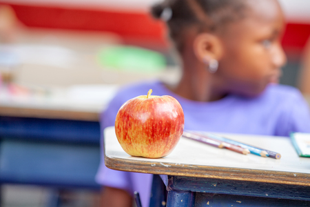 Apple on the desk with african pupil on background.の写真素材