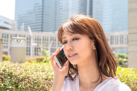 Happy asian girl talking at smartphone and smiling along city streets.の写真素材