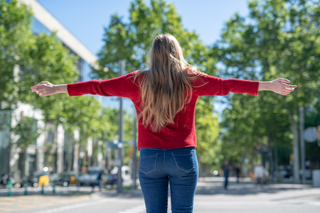 Back view of blonde girl with open arms symbolically embracing the city.の写真素材