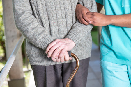 Elderly man with walking stick moving with nurse, detail on the hands.の写真素材
