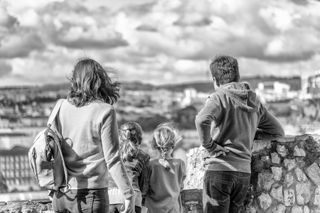 Family of four enjoying city view on a beautiful day. Back view of Father, mother and two children looking at panorama.の写真素材