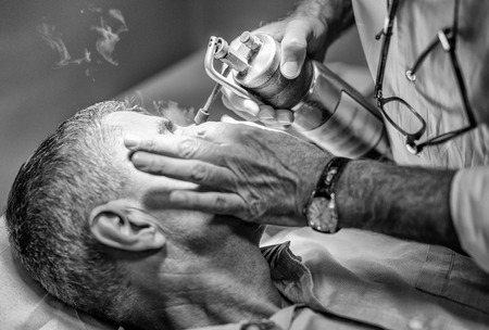 Close up shot of caucasian man in the 50s getting laser facial treatment in cosmetology clinic. Male receiving local cryotherapy therapy.の写真素材