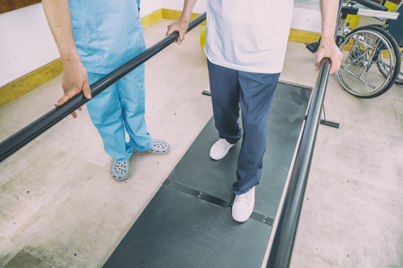 Disabled senior helped by the physiotherapist is doing rehabilitation on the footboard.の写真素材