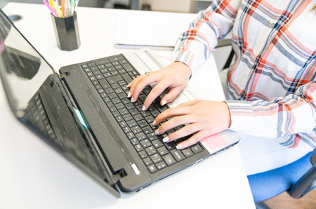 Girl using laptop in the office, focus on fingers and keyboard.