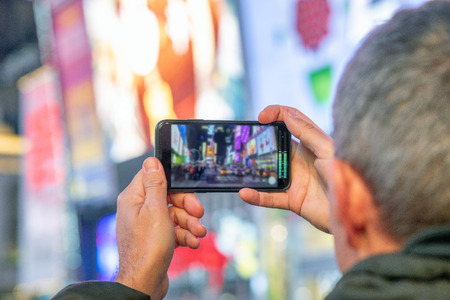 Man taking pictures of Times Square at night with smartphoneの写真素材