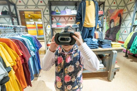 Young girl using VR glasses exploring dress shop.