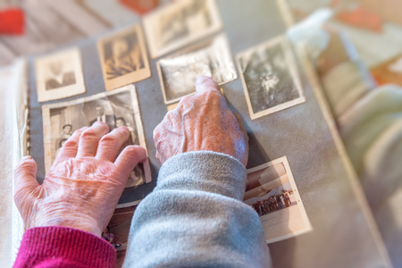 Elderly couple hands looking at old pictures album at home. Detail on hands and old images.の写真素材