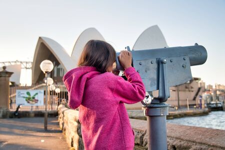Happy smiling young girl visiting Sydney looking into a telescope.の写真素材