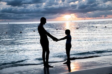 Man with daughter at sunset on the ocean shoreline. Holiday and relax concept.の写真素材