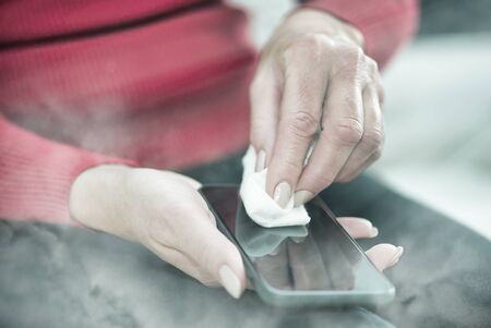 Woman cleaning smartphone at home. Coronavirus prevention against virus outbreak.の写真素材