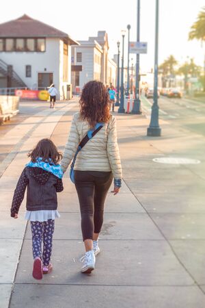Woman with her daughter walking along the oceanfront, back view.の写真素材