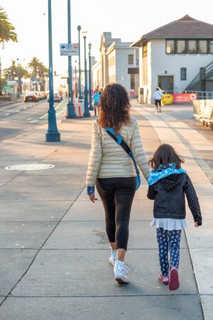 Woman with her daughter walking along the oceanfront, back view.の写真素材