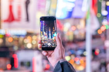 NEW YORK CITY - DECEMBER 2018: Hand holding a smartphone at night in Times Square making panoramic pictures.の写真素材