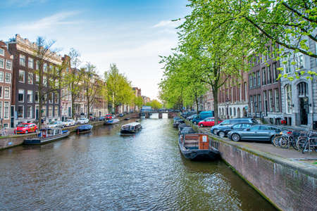 AMSTERDAM, THE NETHERLANDS - APRIL 25, 2015: Traditional houses and buildings on the canal with boats on the water.の写真素材