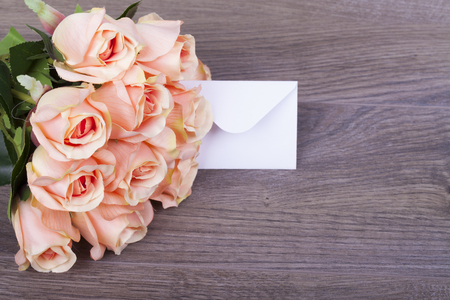 Beautiful roses with a note in the envelope on a wooden baseの写真素材