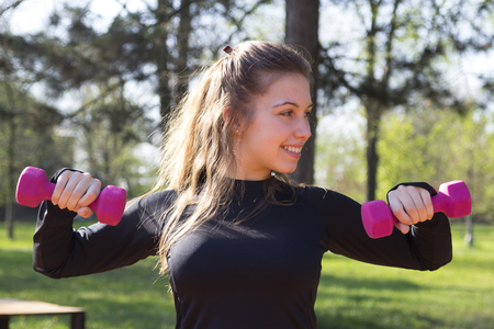 Beautiful young woman doing exercise with weights in the park. Selective focus and small depth of field.の写真素材