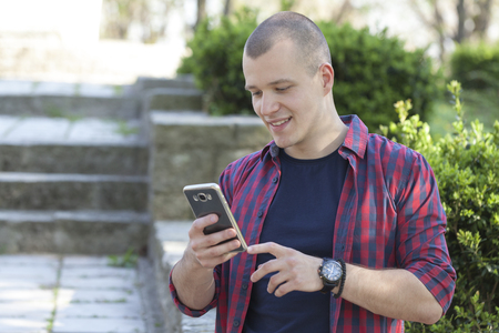 Handsome young man holding phone and enjoy the outdoors. Selective focus and small depth of field.の写真素材