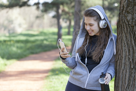 Beautiful young woman using a mobile phone and resting during exercise in the park. Selective focus and small depth of field.の写真素材