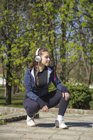 Beautiful young woman doing exercises and enjoys listening to music in the park. Selective focus and small depth of field.の写真素材