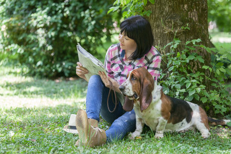 Beautiful smiling woman sitting on the grass in the park with your dog and read newspapersの写真素材
