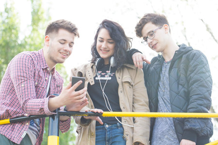 Three smiling young people talk and have great fun. Viewing images on r mobile phone. Lens flare.