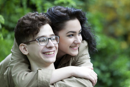 Young love smiling couple in the park. Girl embracing the guy and look very happy.の写真素材