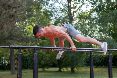 Young muscular young man doing exercises on the parallel bars in the park