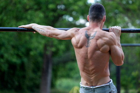 Young fit man doing exercises on the horizontal bar. His muscles are prominent