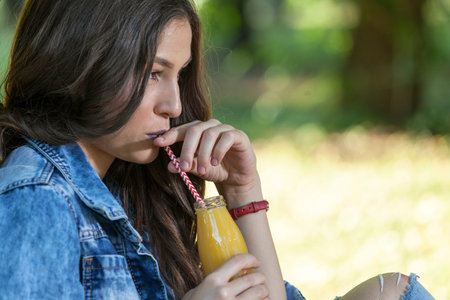 Portrait of a young beautiful woman who is sitting next to the tree and drinking juice. Relax and enjoy natureの写真素材