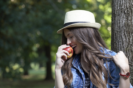 Young woman with a hat enjoying nature and eating an appleの写真素材