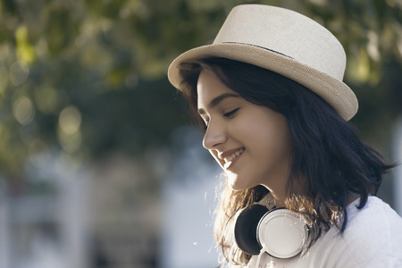 Portrait of smiling beautiful girls, teenagers, with a hat and headphones in the cityの写真素材