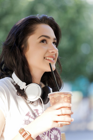 Portrait of a beautiful smiling young girl, teenager, with headphones. She drinks her favorite refreshing drink, lemonade and enjoys itの写真素材