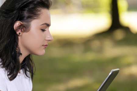 Portrait of a young girl, teenager, with a beautiful face while holding a tablet. She relaxes in natureの写真素材