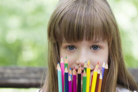 Little girl enjoys a sunny day in the park holding hands crayons. She loves to draw and color with crayons.  School starts soonの写真素材