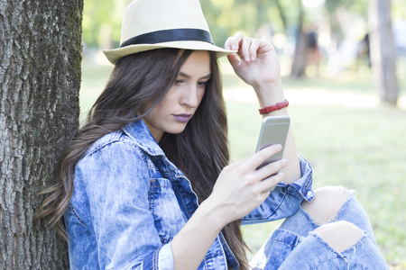 Young beautiful woman with hat  looking on her smart phone outdoors  and enjoy the beautiful dayの写真素材