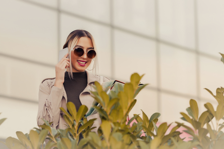 Young attractive happy woman with sunglasses standing in front of the building and talking on the phone.  Copy spaceの写真素材