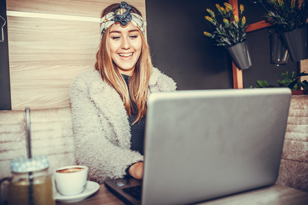 Happy casual beautiful woman watching videos or enjoying entertainment content in a laptop sitting in a coffee shop.の写真素材