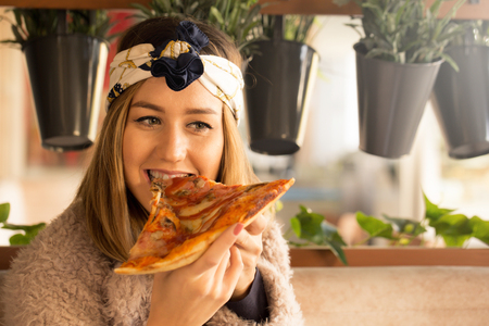 Beautiful happy young woman  eating a slice of pizza in the restaurantの写真素材