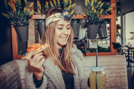 Beautiful happy young woman  eating a slice of pizza and drinking lemonade in the restaurantの写真素材