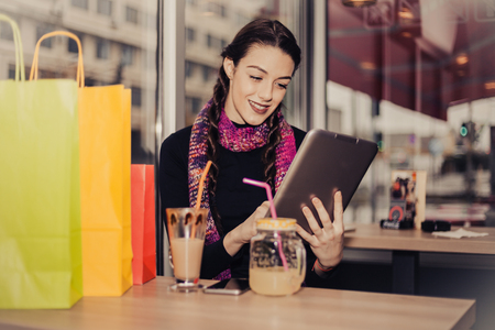 Happy young woman drinking coffee / lemonade and using tablet computer after shopping in a coffee shopの写真素材