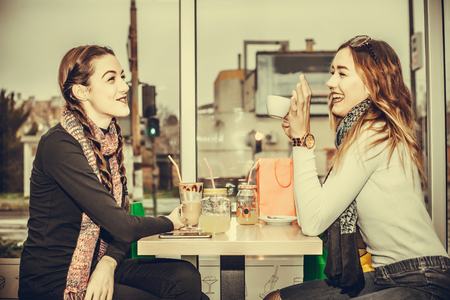 Smiling young women drinking coffee or tea and talking while sitting at the cafe. people, communication and friendship conceptの写真素材