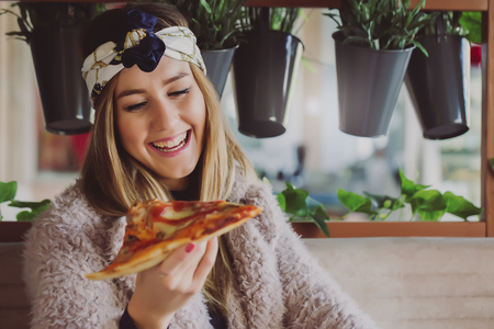 Beautiful happy young woman  eating a slice of pizza in the restaurantの写真素材