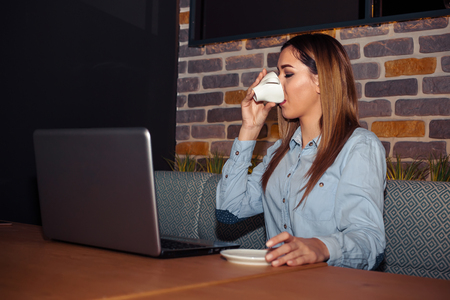 Entrepreneur with a laptop relaxing while drinking caffee and smiling while sitting in a modern cafe interiorの写真素材