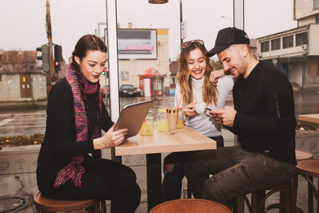 Cheerful group of friends, one man and two women sitting at the table in the cafe shop,  talking and...