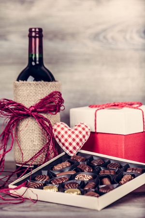 Red wine bottle, box of chocolates and gift with decoration by red heart on wooden table. Valentines day celebration concept. Copy space.の写真素材